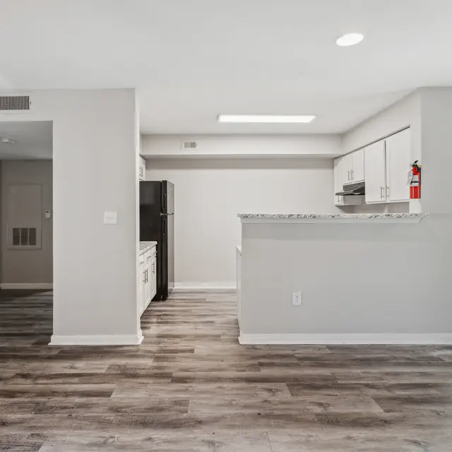 Modern, open-concept living space with gray walls, wood-style flooring, and a kitchen with white cabinets and a granite countertop.