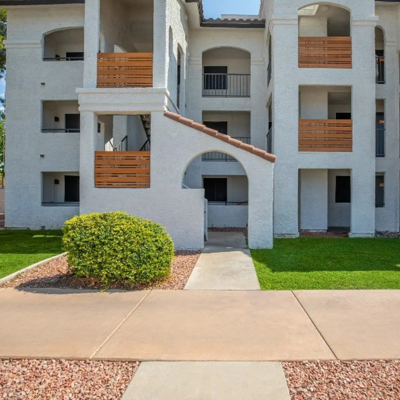 Front view of a multi-story apartment complex with balconies, grassy areas, and a walkway.