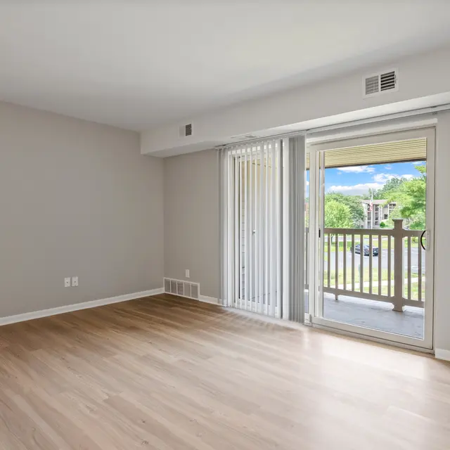 Bright, empty living room with wooden flooring and sliding glass door.