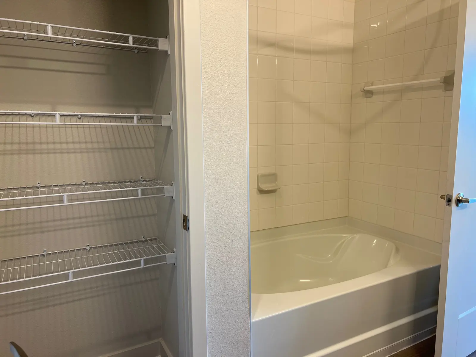 A bathroom area with a bathtub and a separate storage space with wire shelves.