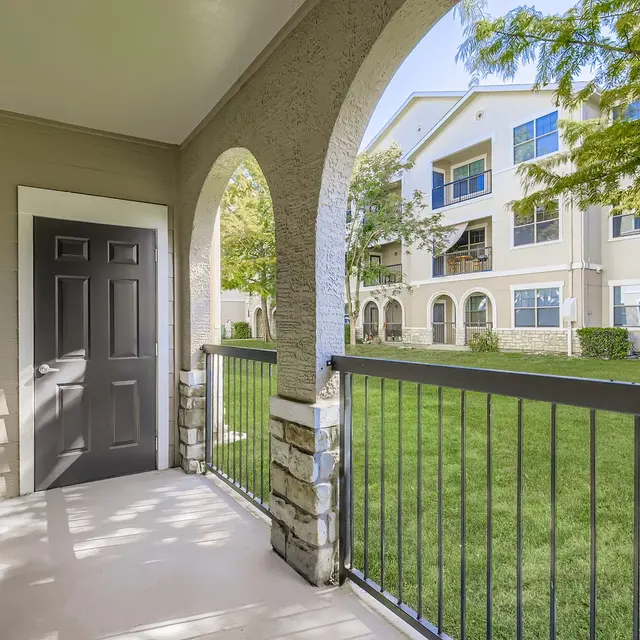 A view from a porch area showcasing an entrance door and landscaped courtyard of an apartment complex.