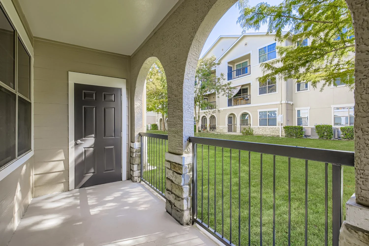 A view from a porch area showcasing an entrance door and landscaped courtyard of an apartment complex.