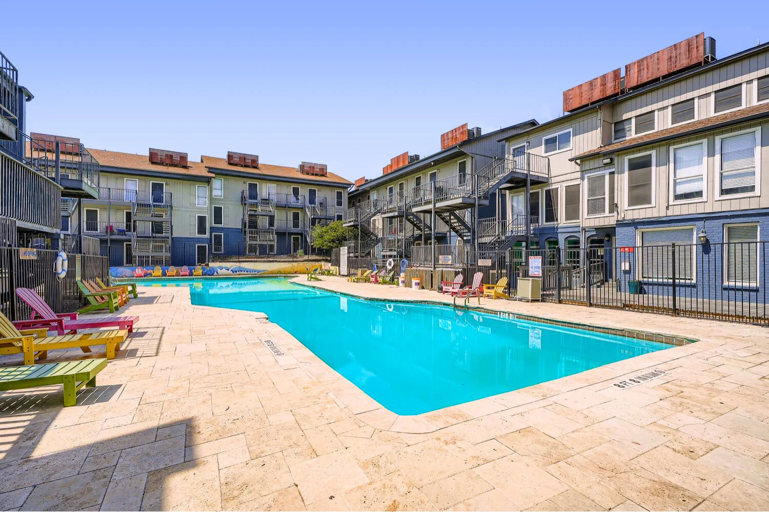 A view of a pool area surrounded by apartment buildings, featuring sun loungers and a well-maintained outdoor space.
