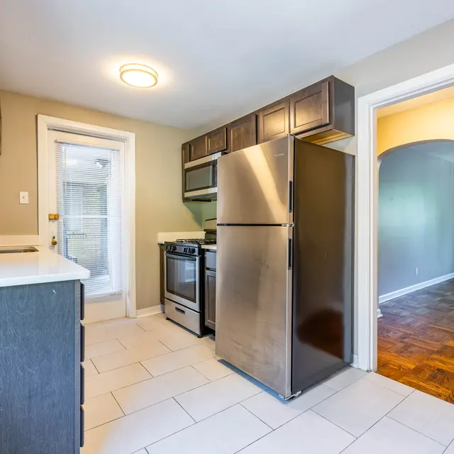 A modern kitchen featuring stainless steel appliances, dark cabinetry, and light tile floors. A door leads to another room outside of the kitchen area.