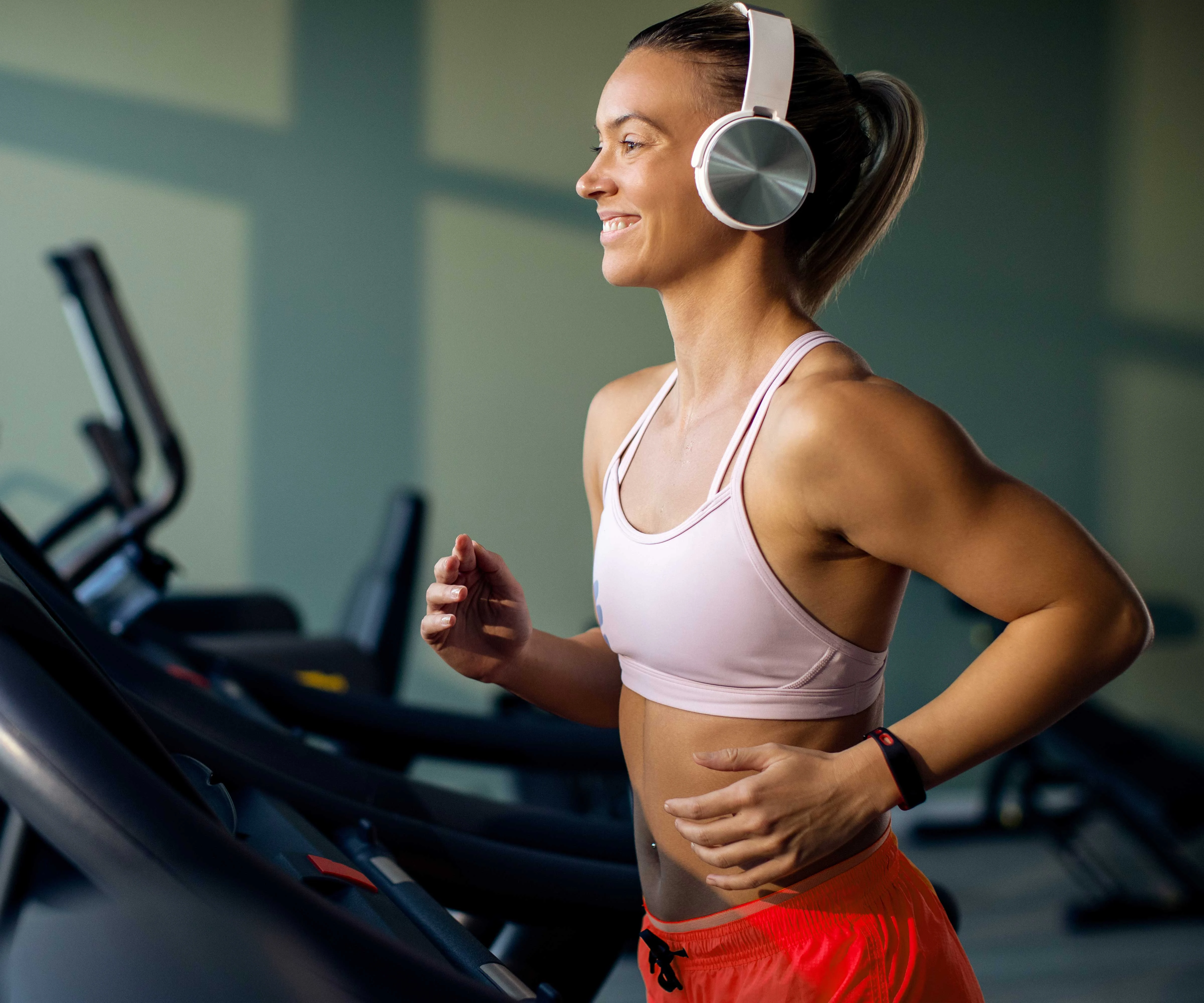 A woman exercising on a treadmill while wearing headphones, smiling and enjoying her workout.