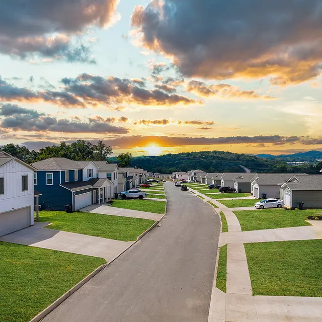 Sunset Over Residential Neighborhood Aerial view of a residential neighborhood during sunset, showcasing houses lining a curved road with mountains in the background.