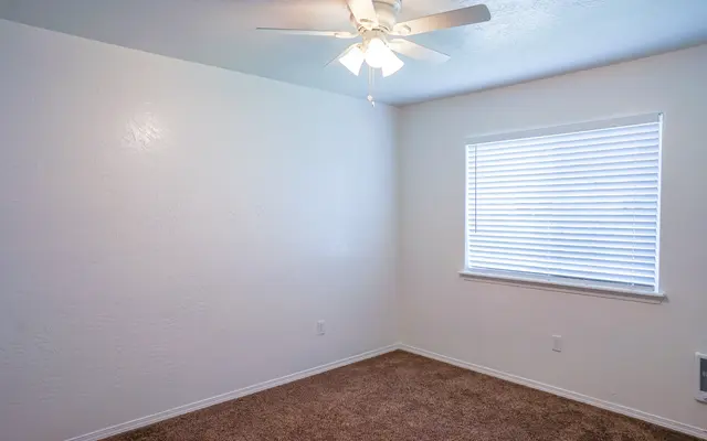 Empty Room with Ceiling Fan and Window An empty room with light-colored walls, a ceiling fan, and a window with white blinds.
