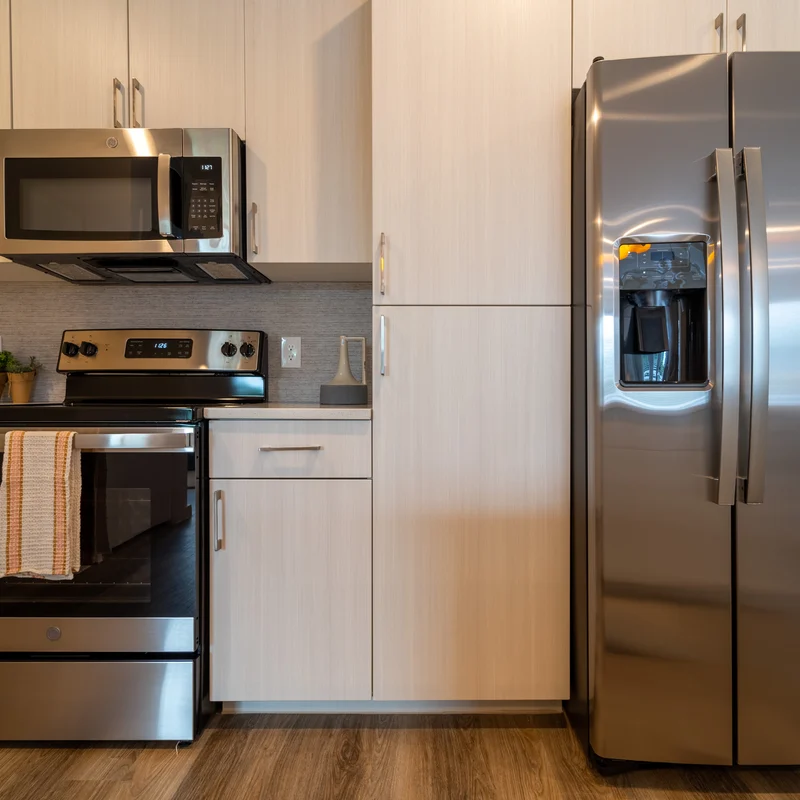 Modern Kitchen with Stainless Steel Appliances A modern kitchen featuring stainless steel appliances including a microwave, oven, and a refrigerator, with light wood cabinetry and a dark countertop.