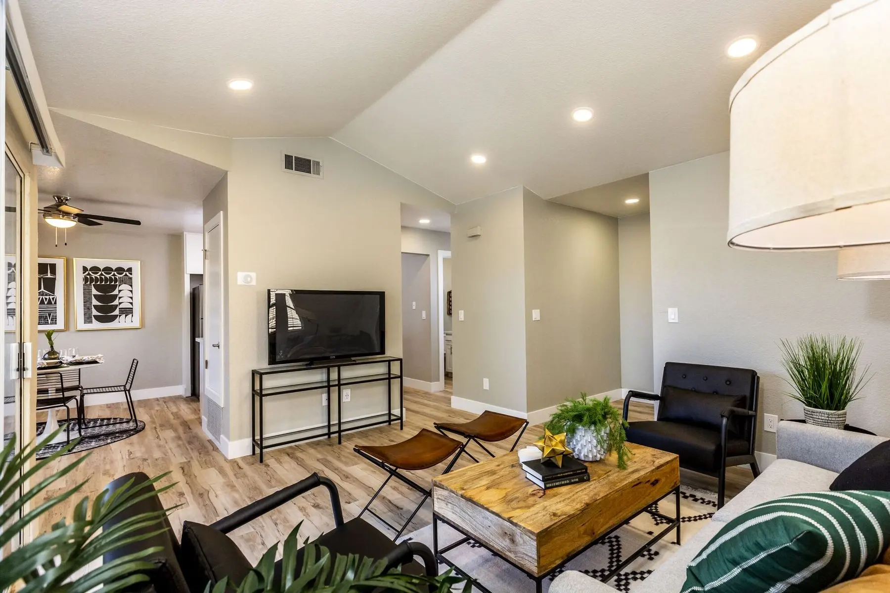 Stylish modern living room with wooden coffee table, black chairs, and decorative plants. Neutral walls and contemporary decor create a welcoming atmosphere.
