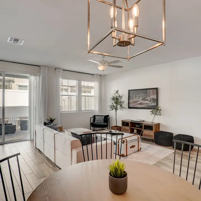 Modern Living Room Interior Bright modern living room with a dining area, featuring white furniture, a circular wooden dining table, and large windows letting in natural light.