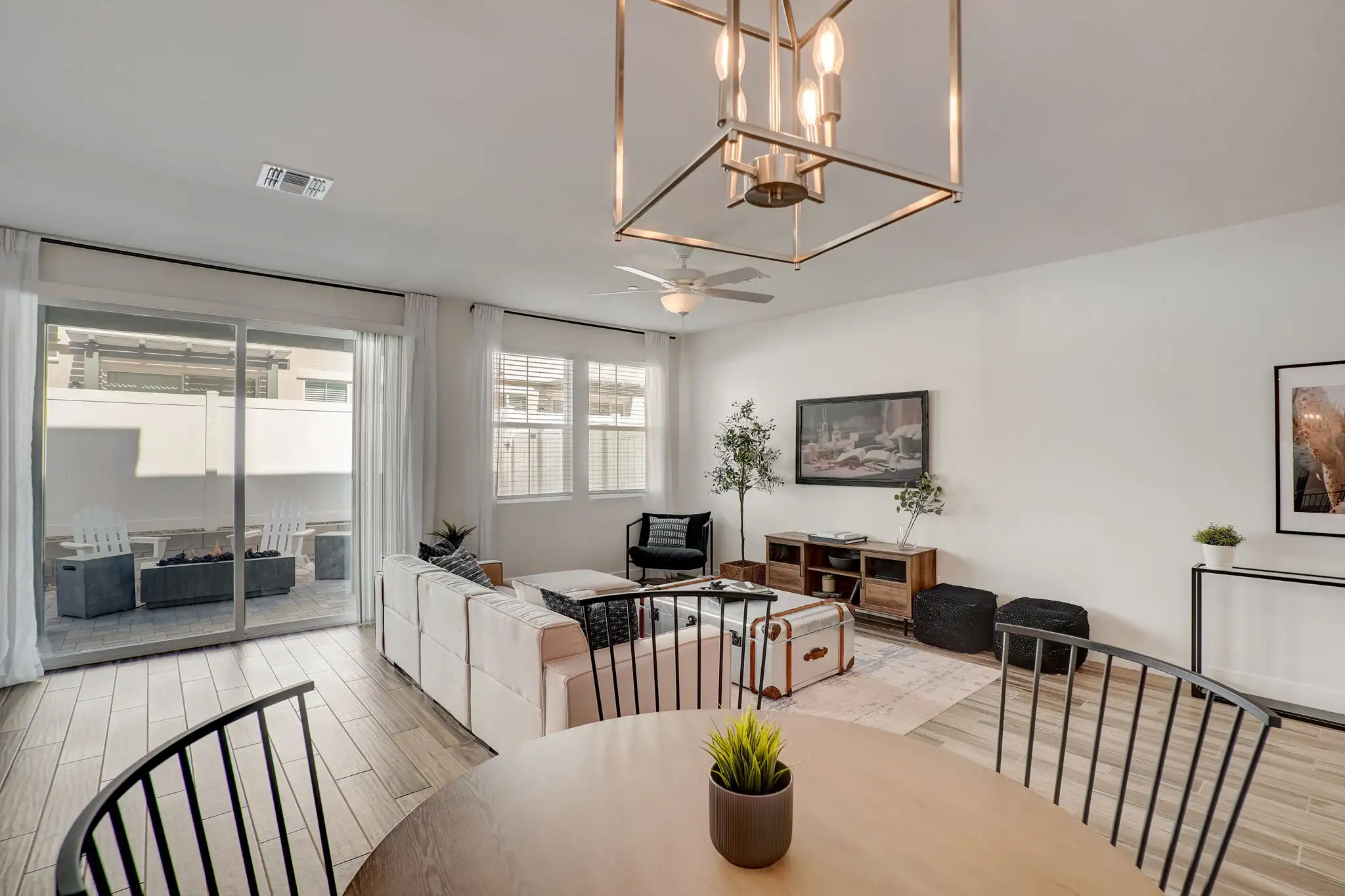Bright modern living room with a dining area, featuring white furniture, a circular wooden dining table, and large windows letting in natural light.