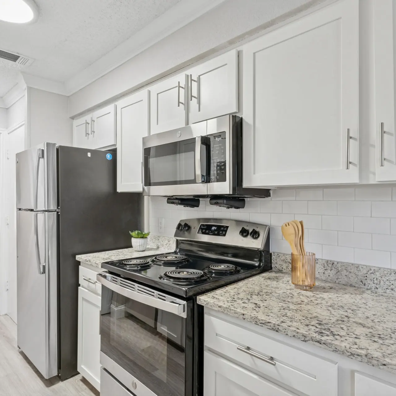 A modern kitchen featuring white cabinets, stainless steel appliances, and a granite countertop.