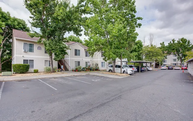 View of an apartment complex with parking area and surrounding trees.