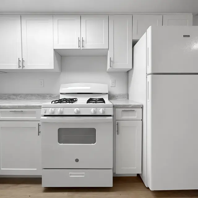 Modern White Kitchen A modern kitchen featuring white cabinets, a gas stove, and a refrigerator. The kitchen has a clean, minimalist design with light wood flooring.