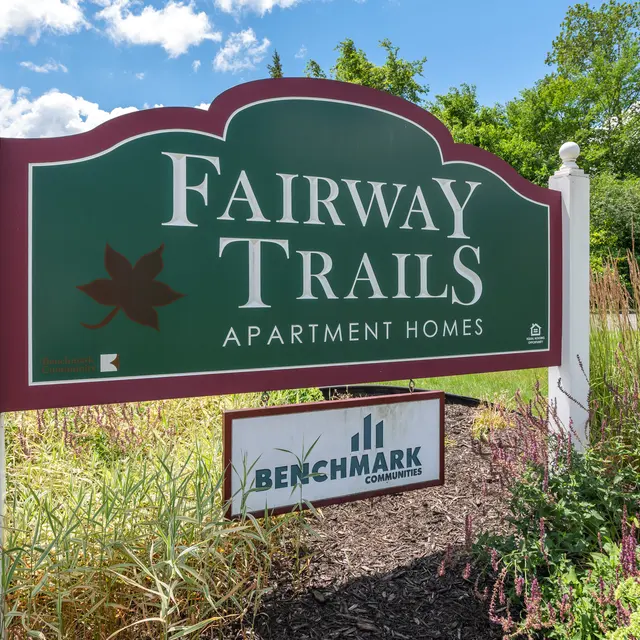 Sign for Fairway Trails Apartment Homes with lush green surroundings and clear blue sky
