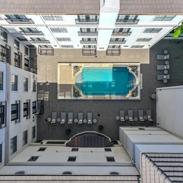 Aerial view of a hotel courtyard featuring a rectangular swimming pool surrounded by lounge chairs. The area is enclosed by buildings on all sides, with several windows visible.