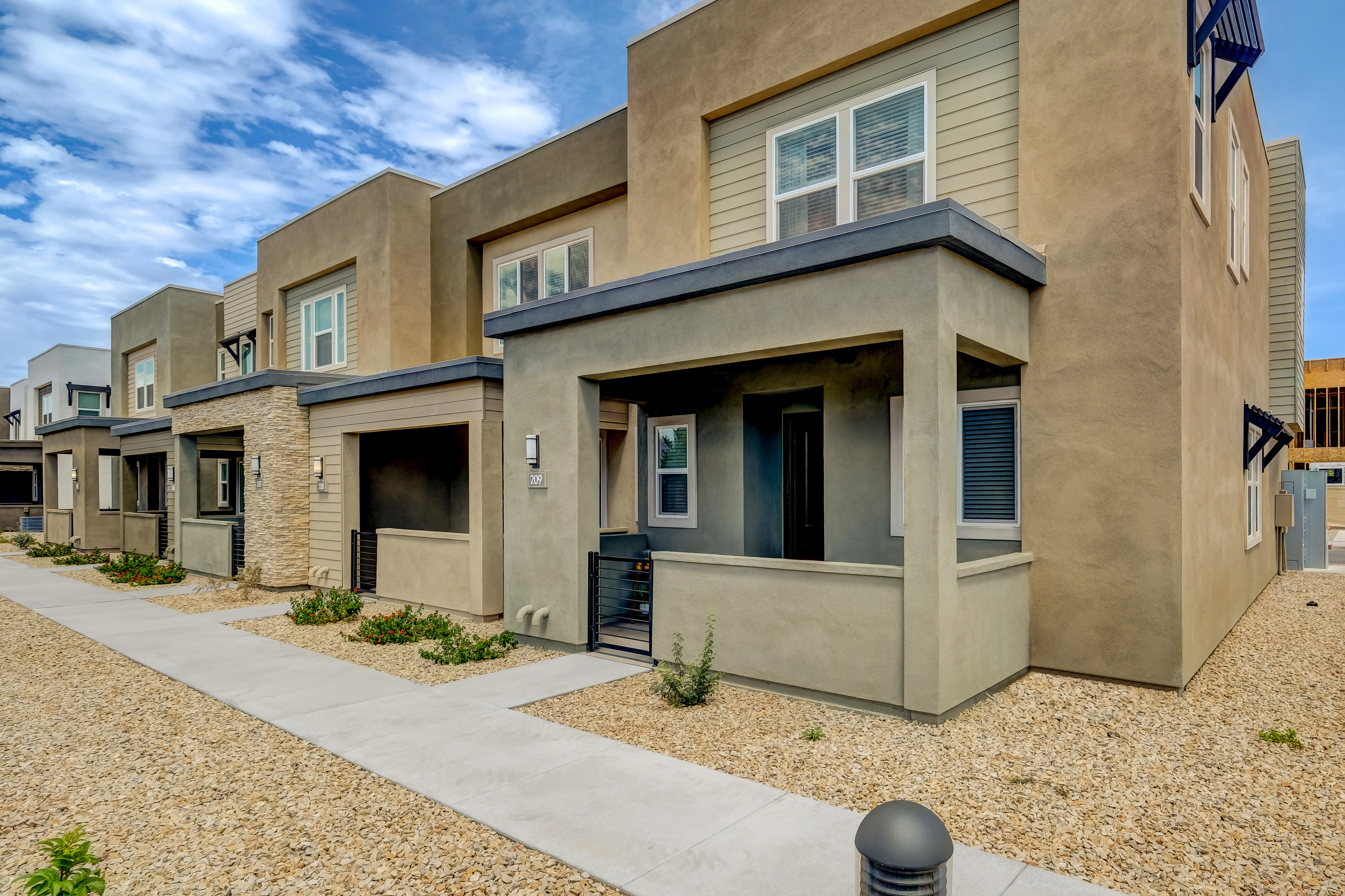 Contemporary Housing Complex A modern housing complex featuring multiple two-story buildings with a mix of stucco and stone facades, surrounded by a landscaped pathway with gravel and greenery.