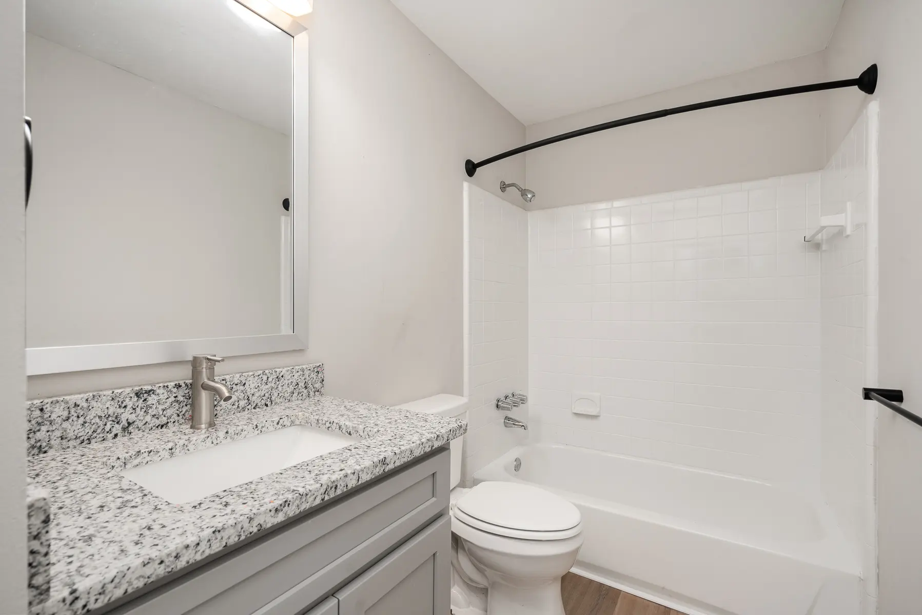 A modern bathroom featuring a granite countertop, a clean white bathtub with a shower, and neutral walls.