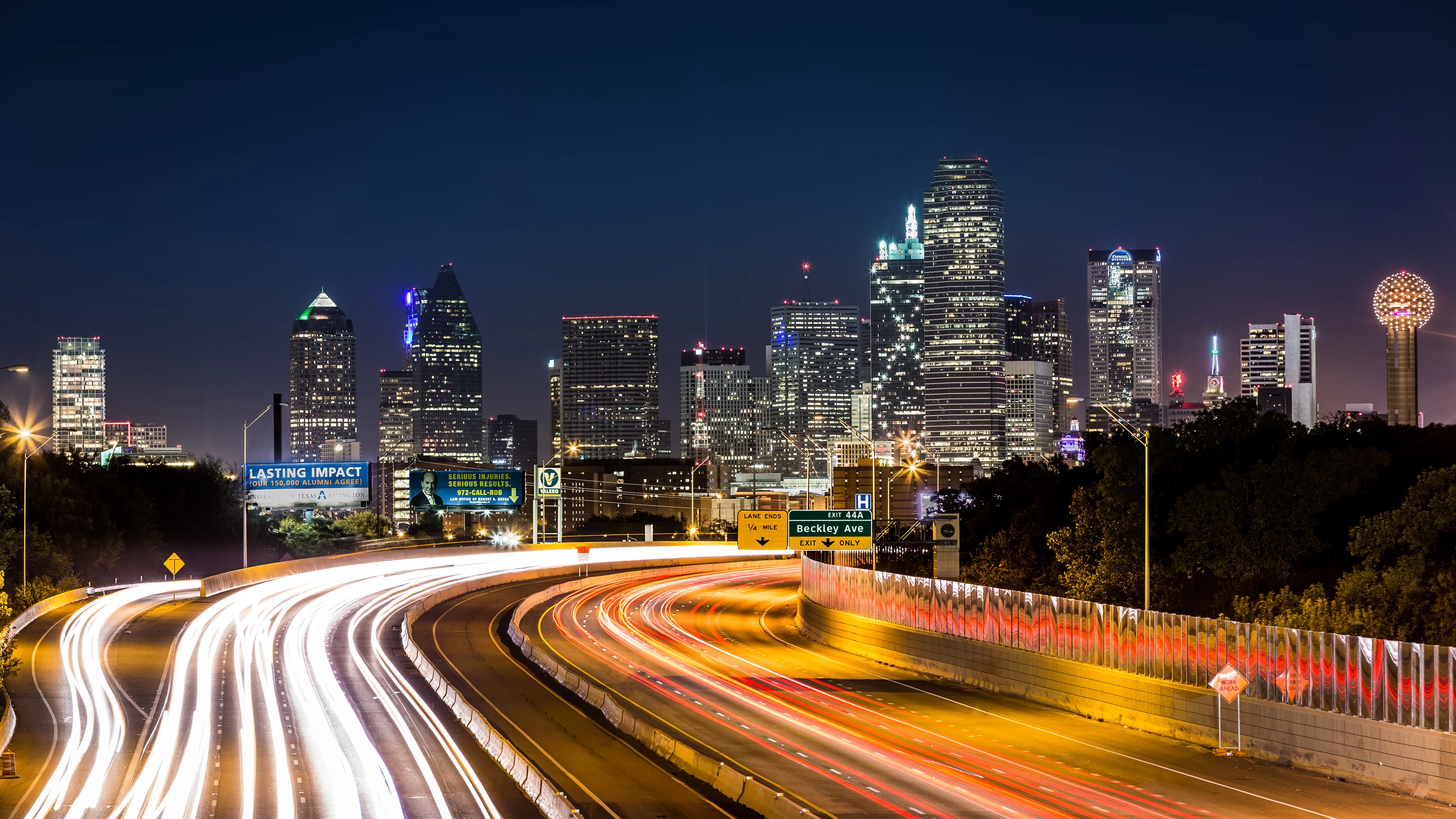 Night view of the Dallas skyline with traffic lights on the highway in the foreground.