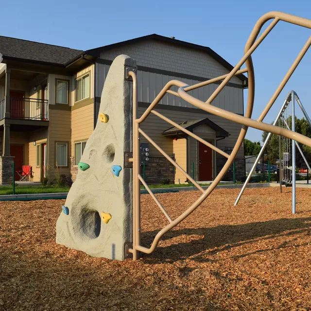 Playground Climbing Structure Near Apartments A playground featuring a climbing wall and swings with an apartment building in the background.