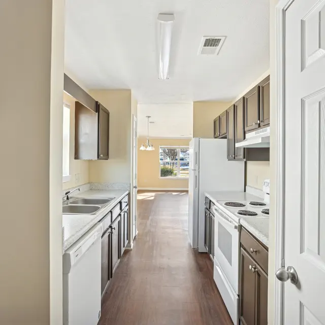 Modern Kitchen Interior A narrow kitchen view showing wooden cabinets, stainless steel appliances, and a clean countertop with a window allowing natural light.