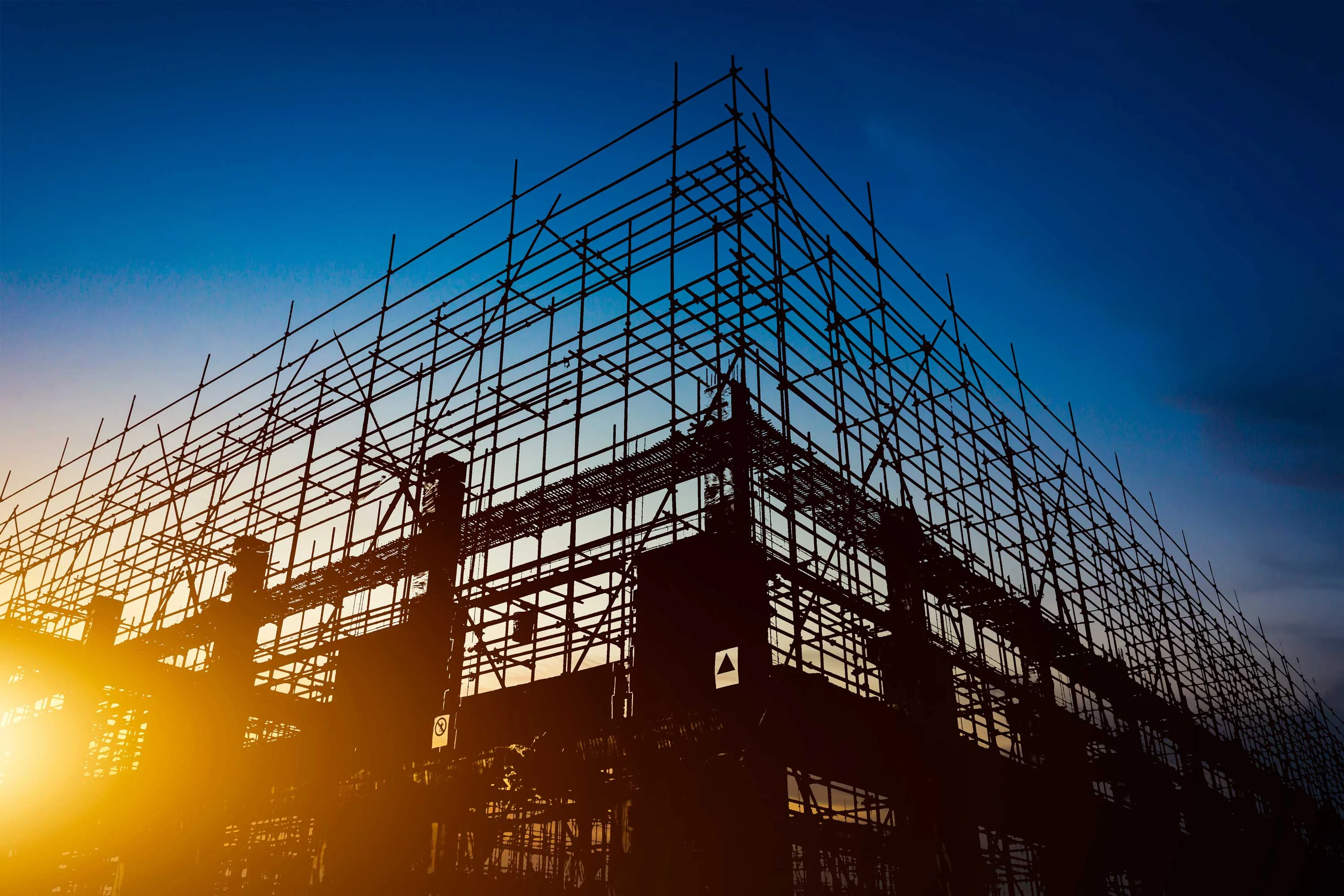 Silhouette of a construction site with scaffolding against a sunset sky.