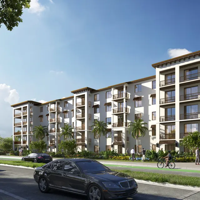 A modern residential apartment building featuring four floors with balconies, palm trees, and surrounding greenery under a clear blue sky.