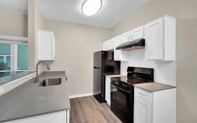A modern kitchen featuring white cabinets, a black refrigerator, a black stove, and a light countertop. The space is well-lit with a circular ceiling light, and has vinyl flooring.