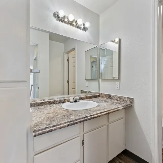 Modern Bathroom Interior A clean bathroom featuring a granite countertop sink, multiple mirrors, and a standing shower.