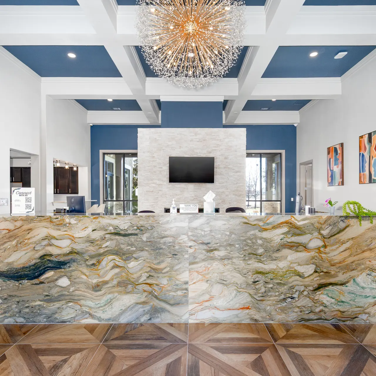A modern reception area featuring a marble front desk, a textured wall with a television, elegant artwork, and stylish light fixtures.