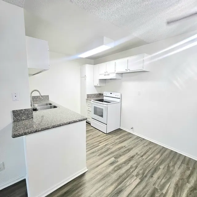 A modern kitchen featuring white cabinets, a gray granite countertop, and stainless steel appliances. The floor is light-colored laminate, creating a bright and inviting atmosphere.