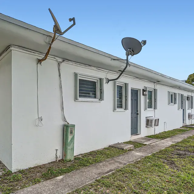 Exterior view of a single-story apartment building with a white facade and several windows.