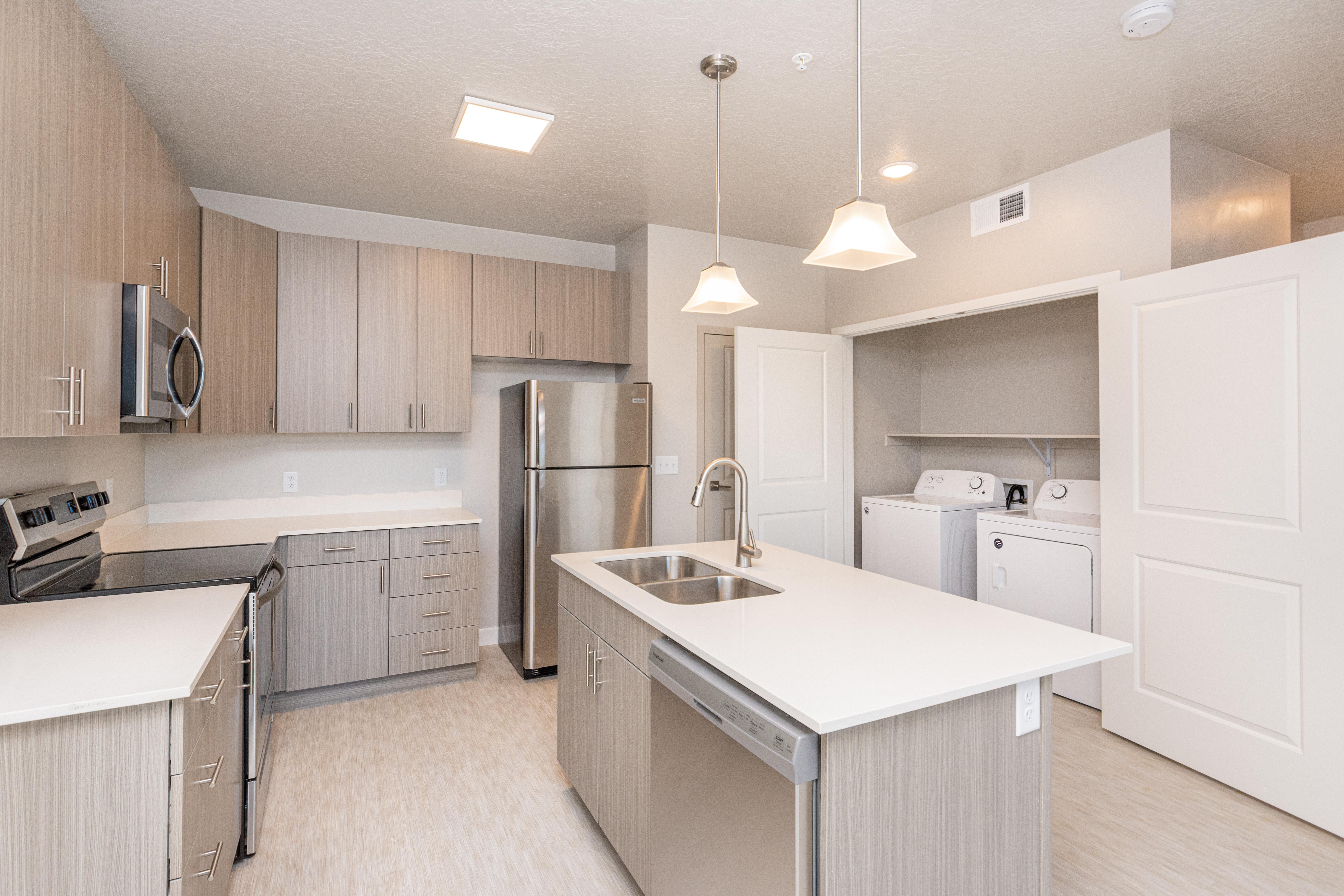 Modern Kitchen with Integrated Laundry Area A modern kitchen featuring wooden cabinetry, stainless steel appliances, and a central island with a sink. There is a laundry area behind a door with a washer and dryer visible.