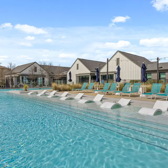 A modern swimming pool area with lounge chairs and a blue sky overhead.