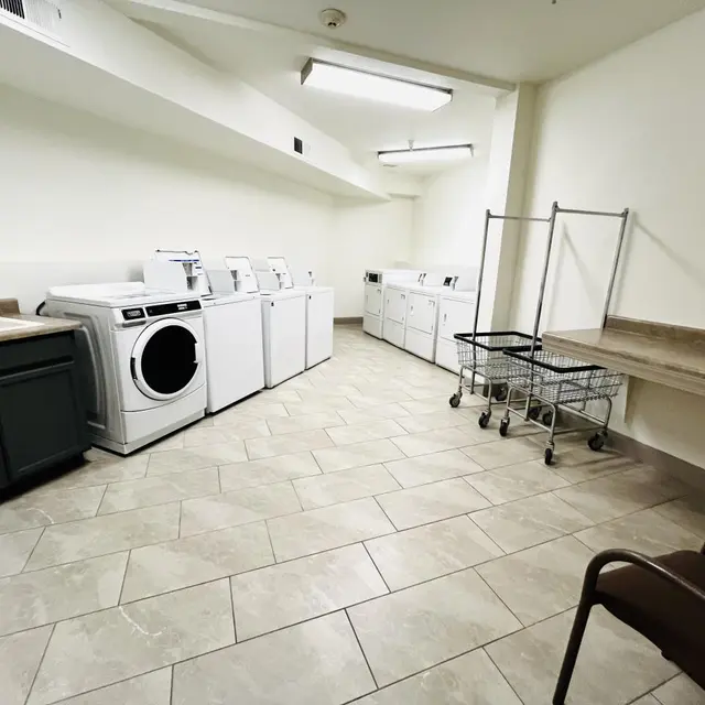 Spacious Laundry Room A clean and spacious laundry room featuring several washing machines, a dryer, a folding table, a laundry cart, and a couple of chairs.