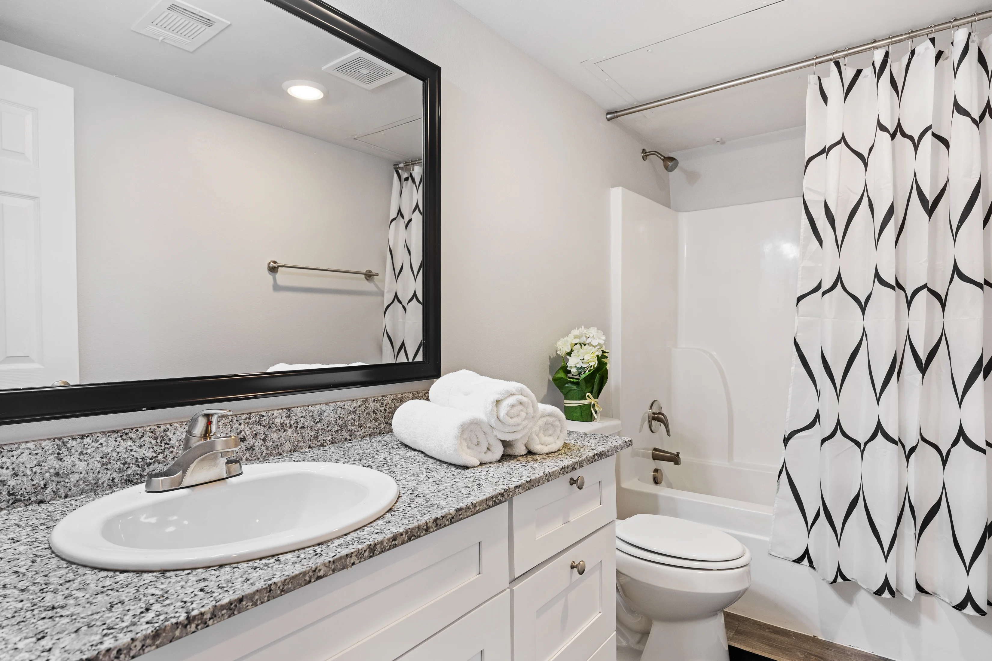Modern Bathroom Interior Design A modern bathroom with a white shower curtain featuring black patterns, a granite countertop sink with white towels neatly arranged, and a small potted plant.