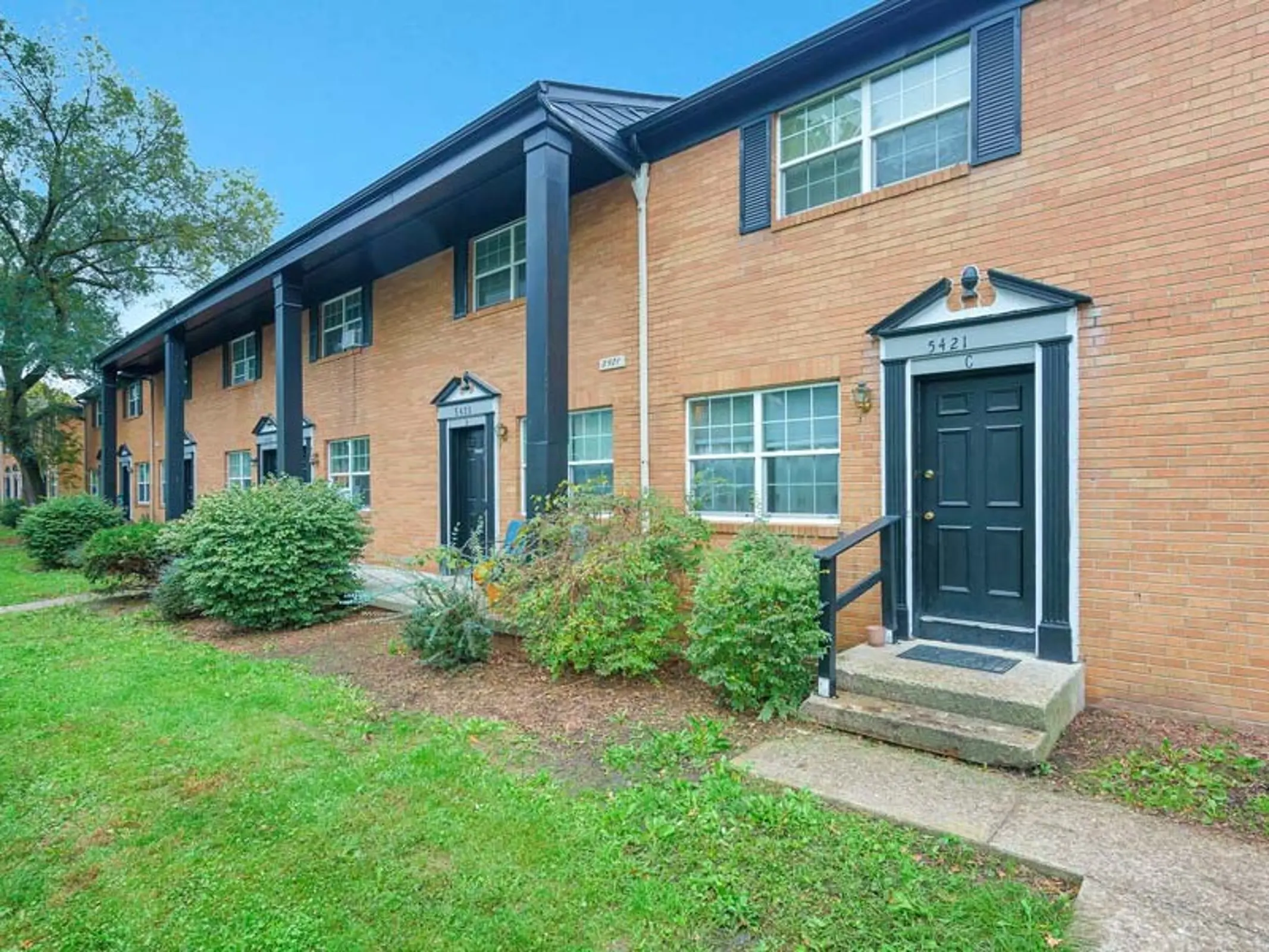 Exterior of Apartment Building Exterior view of a brick apartment building with two levels and black doors, surrounded by greenery.