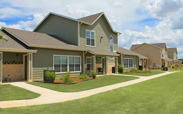 A row of modern houses with green siding and manicured lawns under a partly cloudy sky.