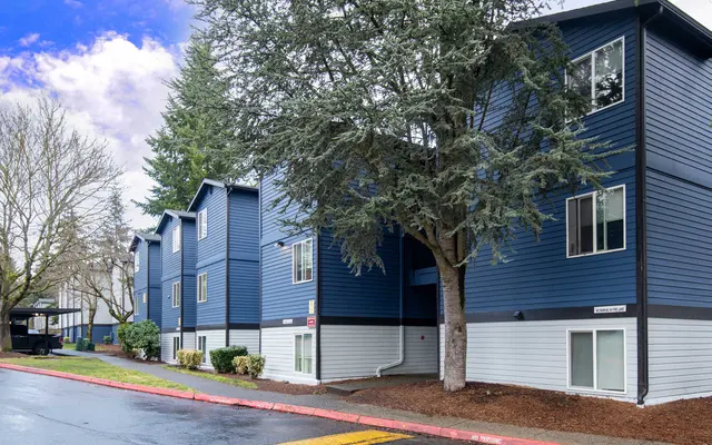 A modern blue apartment building with multiple units, surrounded by trees and a pathway.