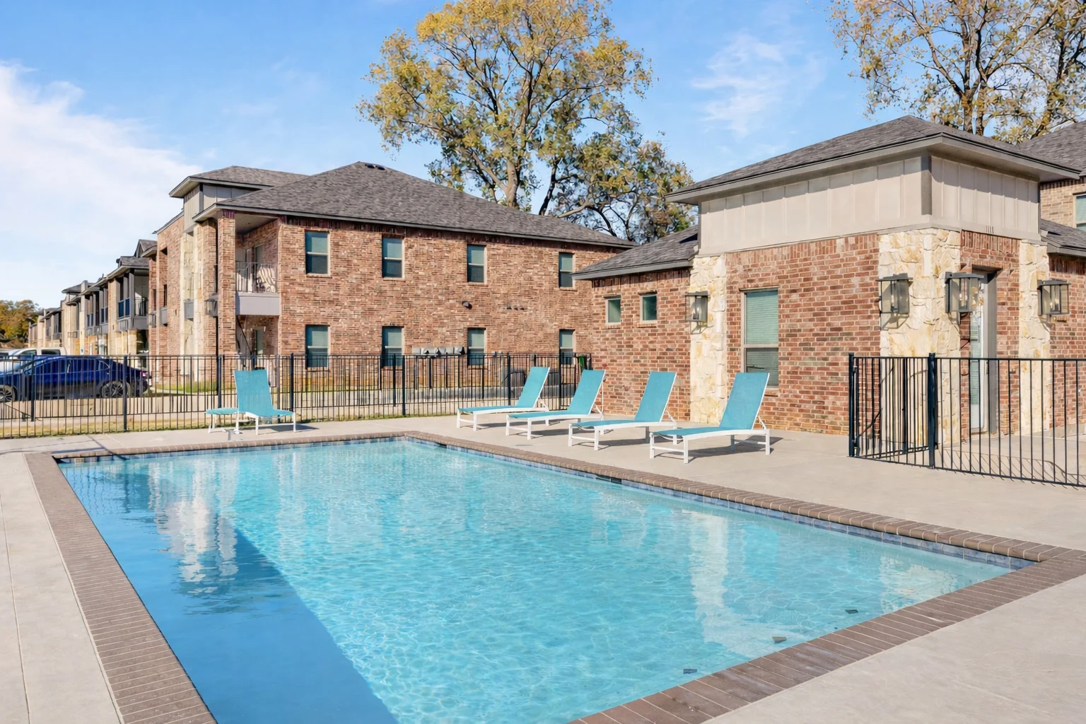 Apartment Complex Pool Area A swimming pool surrounded by lounge chairs in an apartment complex, with brick buildings in the background and clear blue sky.