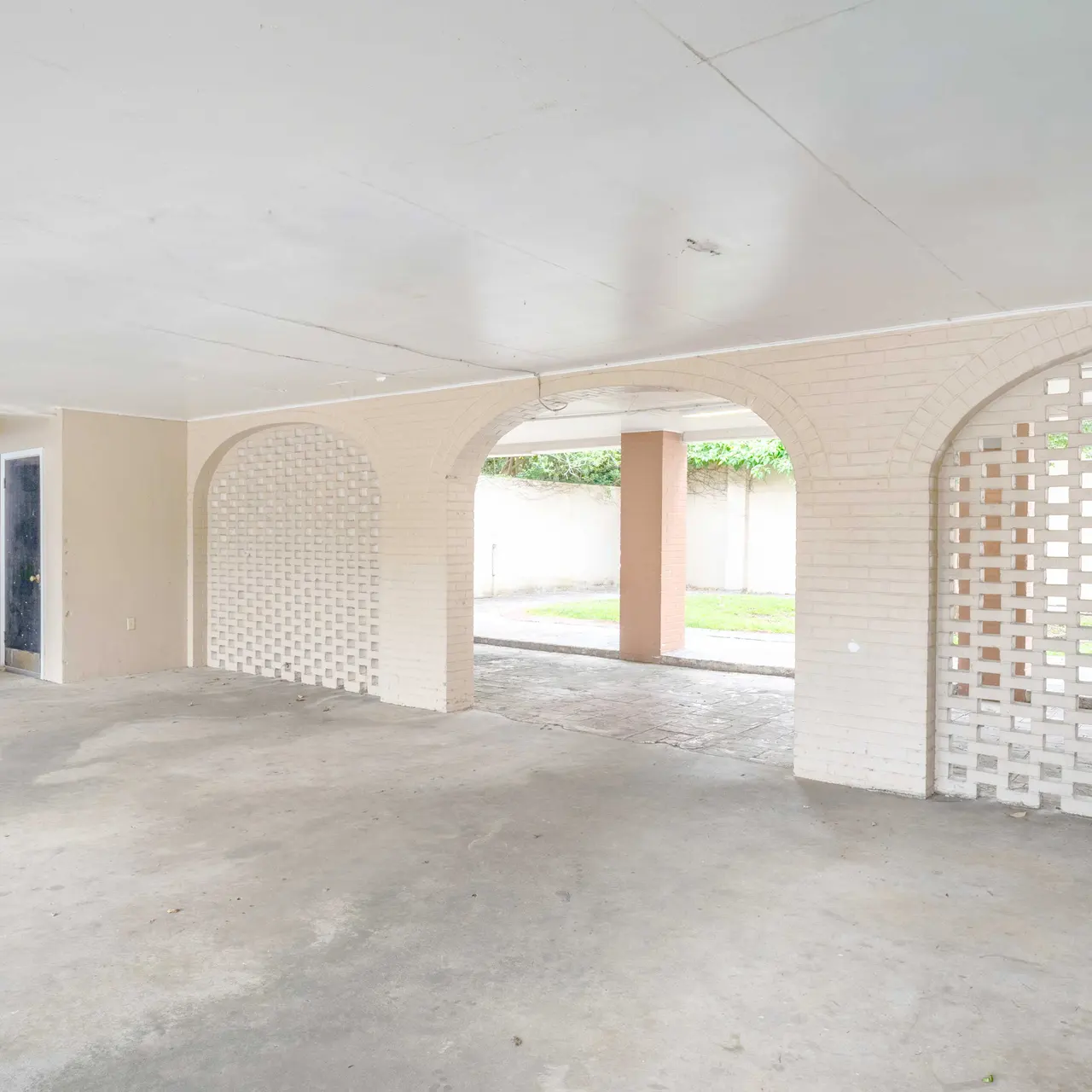 An empty garage with a concrete floor, featuring two decorative archways and a staircase in the corner. Natural light enters through the open space in the background.