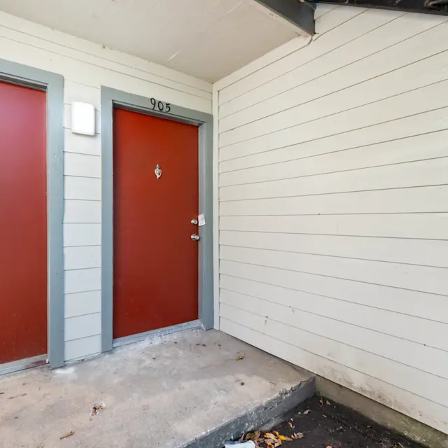 Exterior view of two red doors labeled 903 and 905 at an apartment building entrance, with a small porch area
