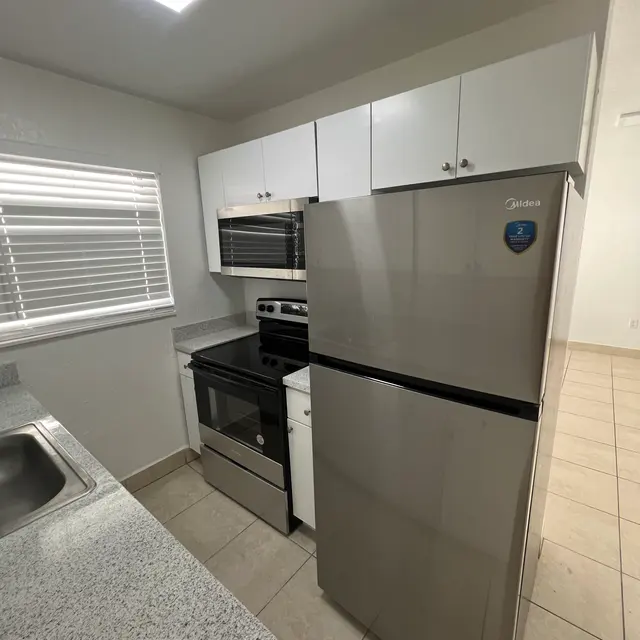 Modern kitchen featuring stainless steel appliances, white cabinetry, and a granite countertop with tile flooring.