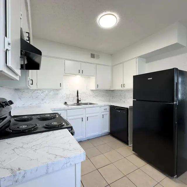 A modern kitchen featuring white cabinets, marble countertops, and black appliances including a refrigerator and stove.