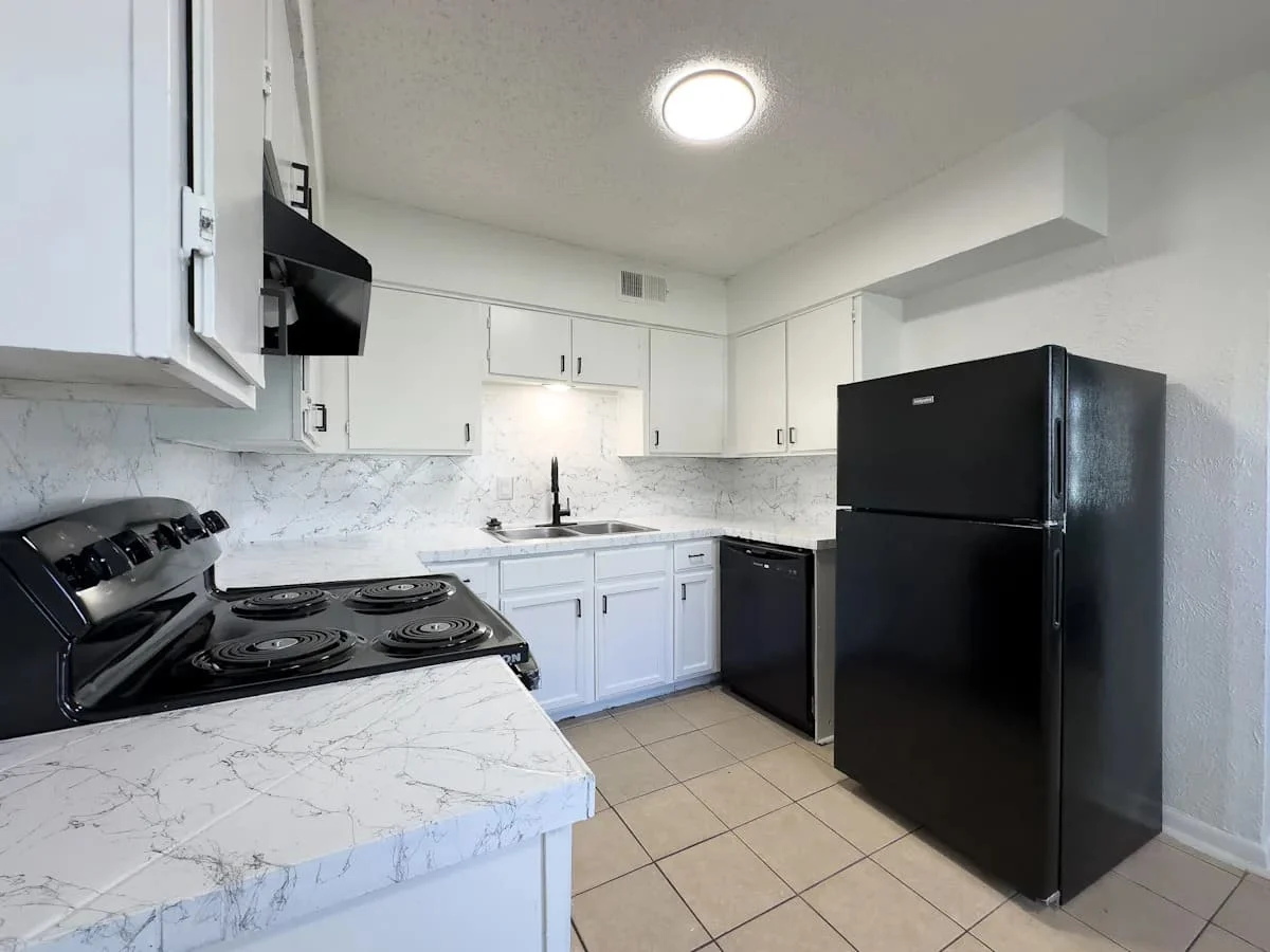 A modern kitchen featuring white cabinets, marble countertops, and black appliances including a refrigerator and stove.