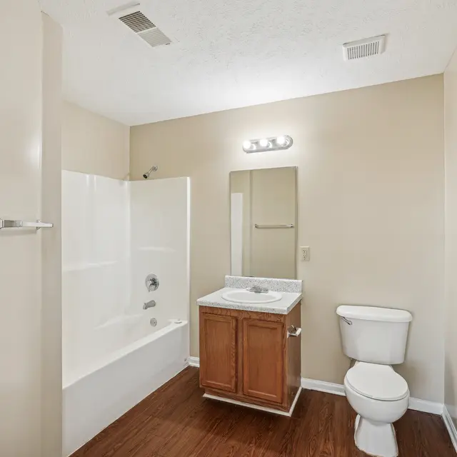 A clean and modern bathroom featuring a bathtub with a shower, a wooden vanity with a sink, a toilet, and neutral-colored walls.