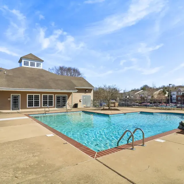 Outdoor swimming pool with a clubhouse beside it on a sunny day.