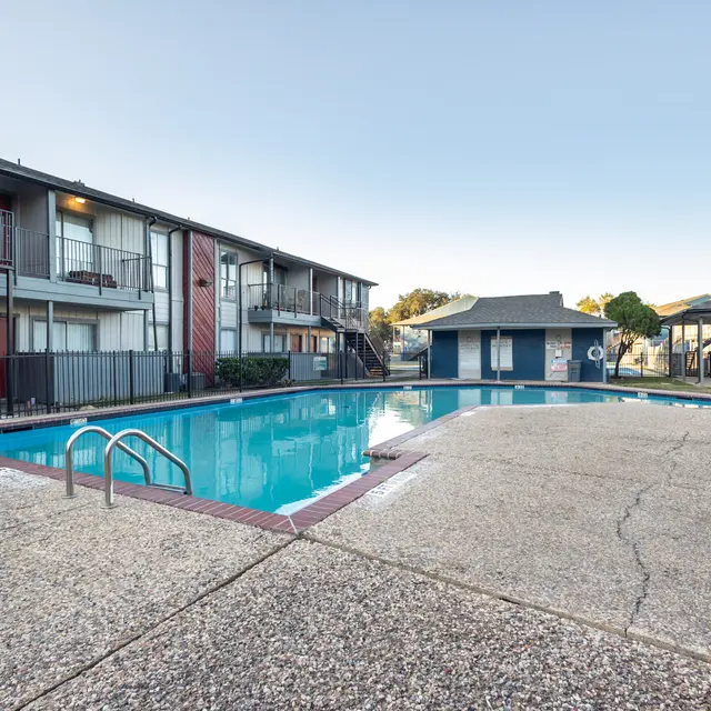 A swimming pool surrounded by apartment buildings, with clear blue water and a concrete deck.
