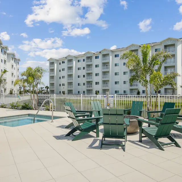 Outdoor Pool Area at Apartment Complex Outdoor pool area with green lounge chairs and a swimming pool, surrounded by greenery and an apartment building in the background.