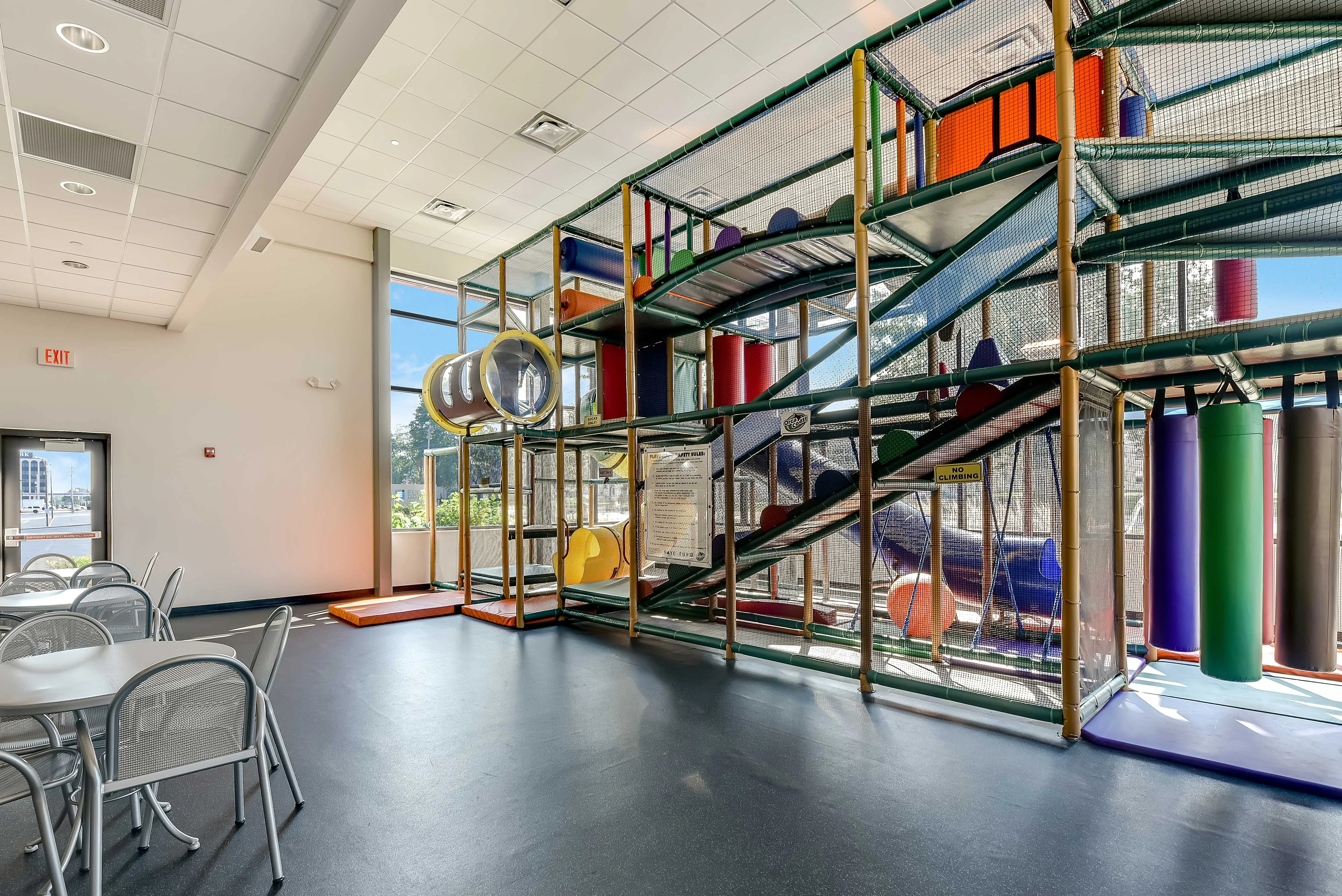 Children's Indoor Play Area An indoor play area featuring a colorful climbing structure with slides and tunnels, surrounded by tables and chairs.